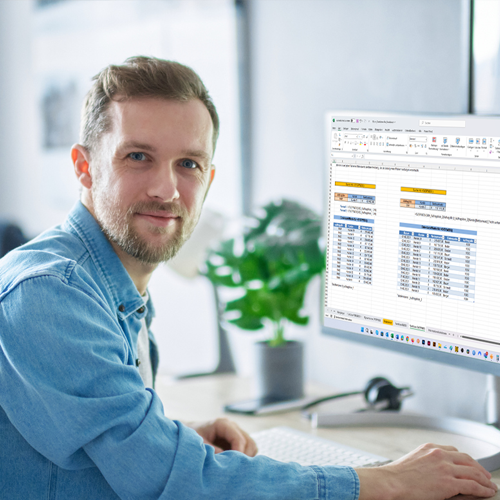 Bild: Junger lächelnder Mann sitzt am Schreibtisch und arbeitet am PC mit Excel
