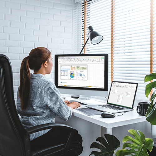 Bild: Junge Frau arbeitet im Büro an einem Computer und zusätzlich an einem Laptop mit Excel