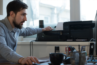 Bild. Ein Mann druckt eine Excel Datei am Tintenstrahldrucker am Schreibtisch aus